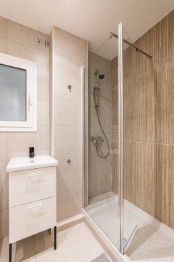 Banyonun köşesinde şeffaf cam duvarla çevrili küçük bir duş alanı var. Tuvalet aksesuarları için çekmeceleri olan bir lavabo. Buzlu cam ve beyaz çerçeveli duvardaki pencere