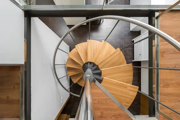 Modern spiral staircase with wooden steps and metal railings looking down from above creates a feeling of weightlessness. Stylish staircase with beautiful architecture in houses with trendy design