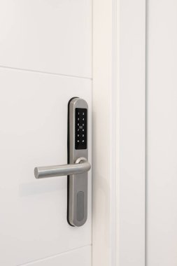 Evin güvenliği için elektronik kilidi olan beyaz ahşap bir kapı. Kilitte kodu girmek için numaraların olduğu düğmeler var. Krom metal kilit