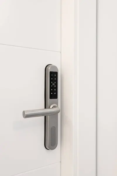 Entrance white wooden door with an electronic lock for the security of the apartment. On the lock there are buttons with numbers for entering the code. Chrome metal lock
