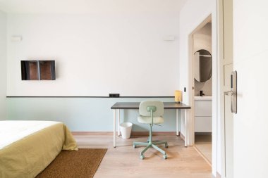 Bej çarşaflı iki kişi için yataklı otel odası. Cam sürgülü kapılardan balkona giriş. Çevrimiçi işler için sandalyeli duvara karşı masa. Duvarda televizyon var, keyifli akşamlarda film izlemek için.