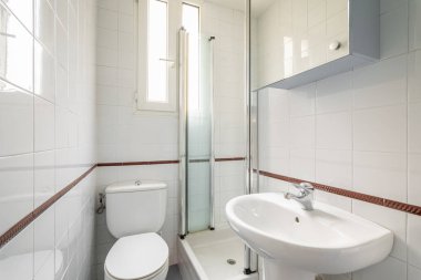 Lüks banyo beyaz seramik fayanslarla kaplı duş tuvaleti ve doğal ışık için dar dikey pencereleri olan lavabo. Küçük ama rahat tuvaletler kavramı.