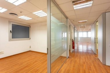 Koridorun sonundaki pencereli boş ofis odasını kapatan cam bölme. Ofis koridorunun ve odanın yenilenmesi gereken modası geçmiş tasarımı. Boş ofis yerinde yanmış floresan lambaları.