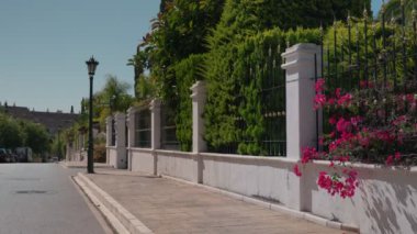 Sessiz bir cadde yemyeşil ağaçların ve renkli begonvillerin açtığı manzaraya açılır..
