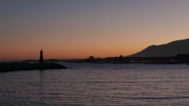Limanda sakin bir akşam, deniz feneri alacakaranlık gökyüzüne karşı duruyor..