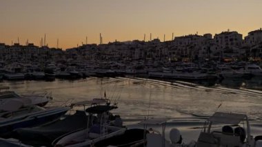 Güneş batıyor, teknelerle dolu bir marinaya altın rengi döküyor, yansımaları suda dans ediyor..