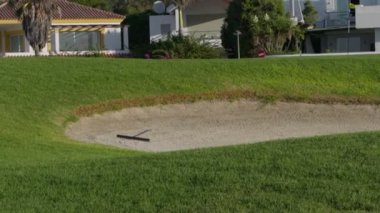 İyi korunmuş bir kursun canlı yeşillikleri arasında bir kum tuzağı golfçüleri bekliyor..