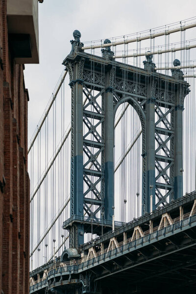 Close-up of the iconic Manhattan Bridge in New York City, showcasing its impressive steel structure and architectural design. The bridge is framed by nearby buildings, capturing essence of urban life.