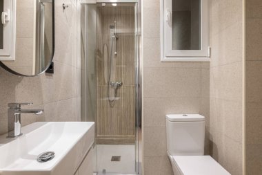 Modern küçük banyo, şık bej fayanslar, cam duş kabini, lavabo, tuvalet ve pencere. Otelde çok işlevli tuvalet kavramı. Genç aile dairesi.