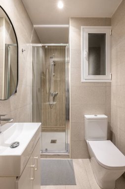 Camdan banyo, lavabo, ayna ve pencereli beyaz tuvalet ile kaplanmış modern bej fayanslı banyo. Otelde ya da küçük bir dairede küçük bir banyo kavramı.