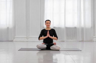 Yoga derslerinde parlak bir odada asma nilüfer pozu veren sağlıklı genç bir kadın. Bu kavram, Budist meditasyonuyla saflığı ve mükemmelliği sembolize eder..