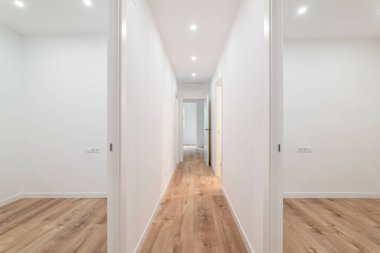 Ahşap zemin, LED ışıklar ve minimalist tasarım ile beyaz bir koridor, modern ve temiz bir alan yaratıyor..