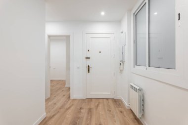 Parlak, modern apartman koridorunda ahşap döşemeler, minimalist beyaz duvarlar ve çağdaş tasarım var.