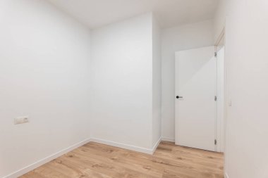 Beyaz duvarları ve ahşap zemini olan parlak, boş bir oda, modern minimalist iç tasarımı sergiliyor..