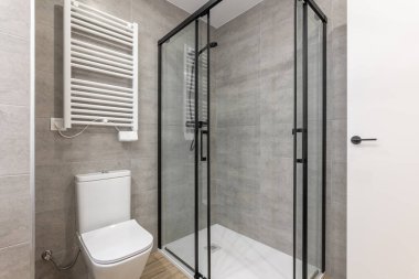 Çağdaş banyo, cam duş muhafazası, ince tuvalet ve minimalist tasarımla ısıtılmış havlu rayı..
