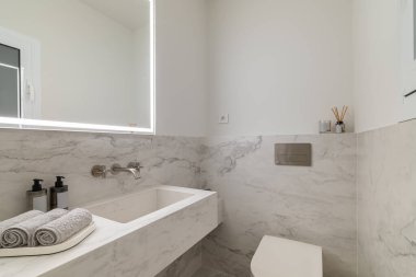 Pürüzsüz mermer kaplamaları, modern demirbaşları ve minimalist dekorları olan şık ve çağdaş bir banyo.