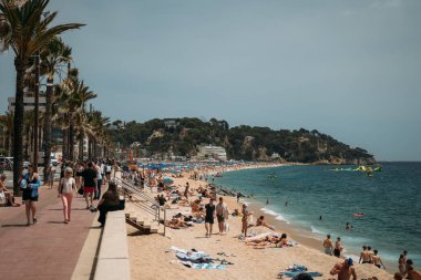 Lloret de Mar, İspanya - 24 Temmuz 2024. İspanya, Costa Brava 'da güneşlenenlerle, palmiyelerle ve çarpıcı kıyı manzaralarıyla dolu canlı bir sahil..