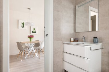 Oturma odasının içi bej renkte, yemek masası ve banyodan büyük dolaplı sandalyeler ve lavabo manzaralı. Şık ve rahat daire tasarımı kavramı.