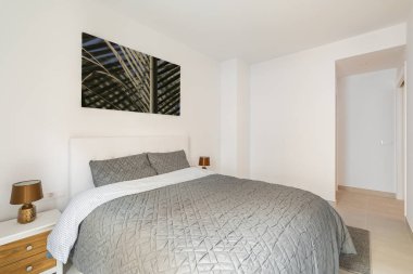 Çift kişilik yataklı, aydınlık duvarlı şık bir yatak odası ve duvarında bir resim. Genç bir çift için dairede minimalist modern tasarım kavramı.