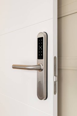 Evin güvenliği için elektronik kilidi olan beyaz ahşap bir kapı. Kilitte kodu girmek için numaraların olduğu düğmeler var. Krom metal kilit