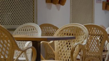 Modern bir kafede ahşap bir masa etrafında şık hasır sandalyeler düzenlenir, davetkar bir atmosfer yaratır.