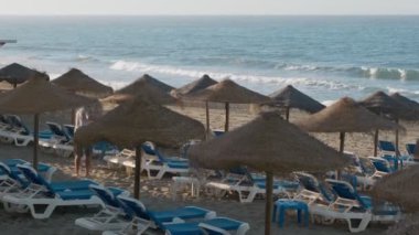 Saman şemsiyeleri ve okyanus kenarındaki rahat mavi şezlonglarla huzurlu sahil ortamının tadını çıkar.