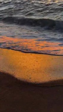 Altın güneş ışığı, yumuşak, kumlu sahille karşılaştıklarında narin, parıldayan okyanus dalgalarından güzel bir şekilde yansıyor.