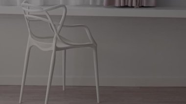 Yumuşak ışıklandırılmış, minimalist bir iç mekânda güzelce sergilenen, sükunet saçan çağdaş beyaz bir sandalye.