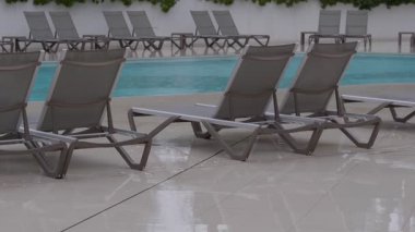 Islak şezlongları ve parlak döşemeleri kaplayan yağmur suyuyla ıssız bir tatil köyü havuzu..