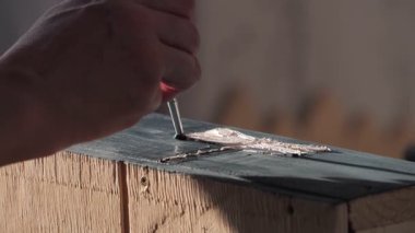 Bir el, ince bir aletle boyanmış bir tahta kutuya dokulu elementler ekliyor..