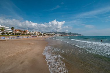 Sitges 'de sakin bir sahil. Dalgalar, altın kum ve dağların manzarası ve kıyı kasabası..