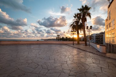 Akdeniz 'in üzerinde nefes kesici bir gün batımı palmiye ağaçlarına altın ışığı ve İspanya' nın Sitges kentindeki taş plazaya vuruyor..