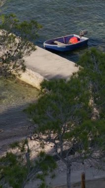 Kıyı boyunca şeffaf turkuaz sularda yüzen, rıhtıma demirli kırmızı yakıt konteynırıyla küçük bir balıkçı teknesi..