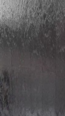 Suyun dokulu siyah taş bir duvardan aşağı akması, yansımaların ve hareketlerin karmaşık bir etkileşimini oluşturur..