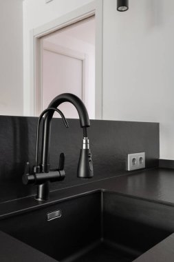 Modern bir evde koyu renkli bir taş tezgahın üzerine kurulmuş siyah bir mutfak musluğunun ayrıntılı bir görüntüsü..