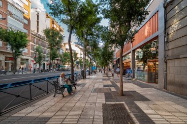 Madrid, İspanya - 13 Temmuz 2019. Madrid 'de canlı bir cadde modern mağazalar, yemyeşil ağaçlar ve şehir atmosferinin keyfini çıkaran yayalar var..