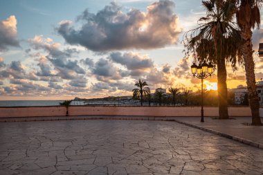 İspanya, Sitges 'de güzel bir gün batımı. Palmiye ağaçlarının arasından süzülen altın güneş ışığı taştan terasa yansıyor..