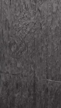 Yüzeyinde su akan, dalgalanmalar ve doğal desenler oluşturan koyu dokulu taş duvarın detaylı görüntüsü..