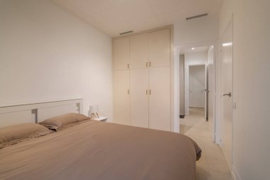 Geniş, minimalist bir yatak odası, bembeyaz bir gardırop ve temiz nötr duvarları var.