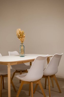 Beyaz sandalyeleri ve kurumuş çiçekli ahşap bir masayı gösteren modern bir yemek salonu.