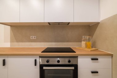 Cam ocağı, ahşap tezgahı, beyaz dolabı ve fayanslı duvarı olan mutfak tezgahının odaklanmış görüntüsü.