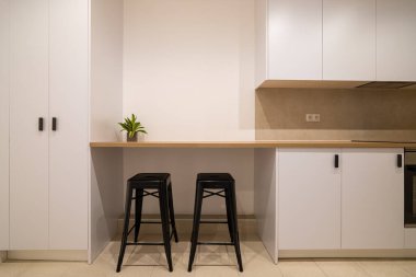 Ahşap tezgahı olan bir mutfak barı manzarası, siyah tabureler ve beyaz dolaplar.