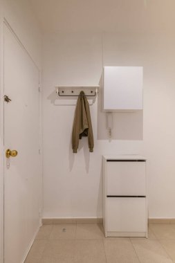 Minimalist giriş. Palto askısı, ayakkabı dolabı ve bej döşemeli beyaz duvarlar.