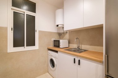 Mutfak köşesinde beyaz dolap, ahşap tezgah, musluk ve mikrodalga fırın gibi kompakt bir lavabo var.