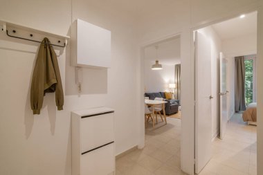 Beyaz duvarları, bej döşemeleri ve diğer odalara açılan kapıları olan basit parlak koridor.