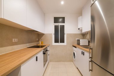 Uzun ahşap tezgahlı kompakt mutfak düzeni, beyaz dolap, fırın, soba ve buzdolabı.