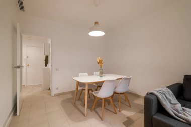 Yemek masası ve sandalyeler koyu gri bir kanepenin yanında küçük bir alana yerleştirilmiş, rahat ve işlevsel bir yaşam alanı oluşturuyorlar.