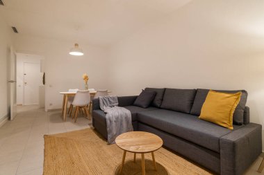 Gri bölmeli kanepesi, hardal yastığı, ahşap masası ve doğal dekorasyon tarzıyla minimalist parlak oturma odası.