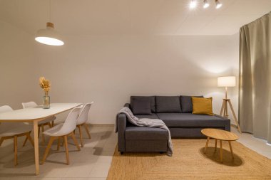 Parlak oturma odası, gri bölmeli kanepe, yuvarlak kahve masası, ve bitişik yemek masası, hoş geldin atmosferi yaratıyor.