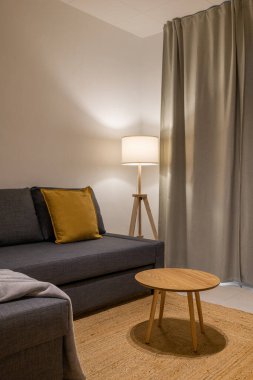 Gri bölüm kanepe, hardal yastık, ahşap sehpa ve pencerenin yanında duran lamba.